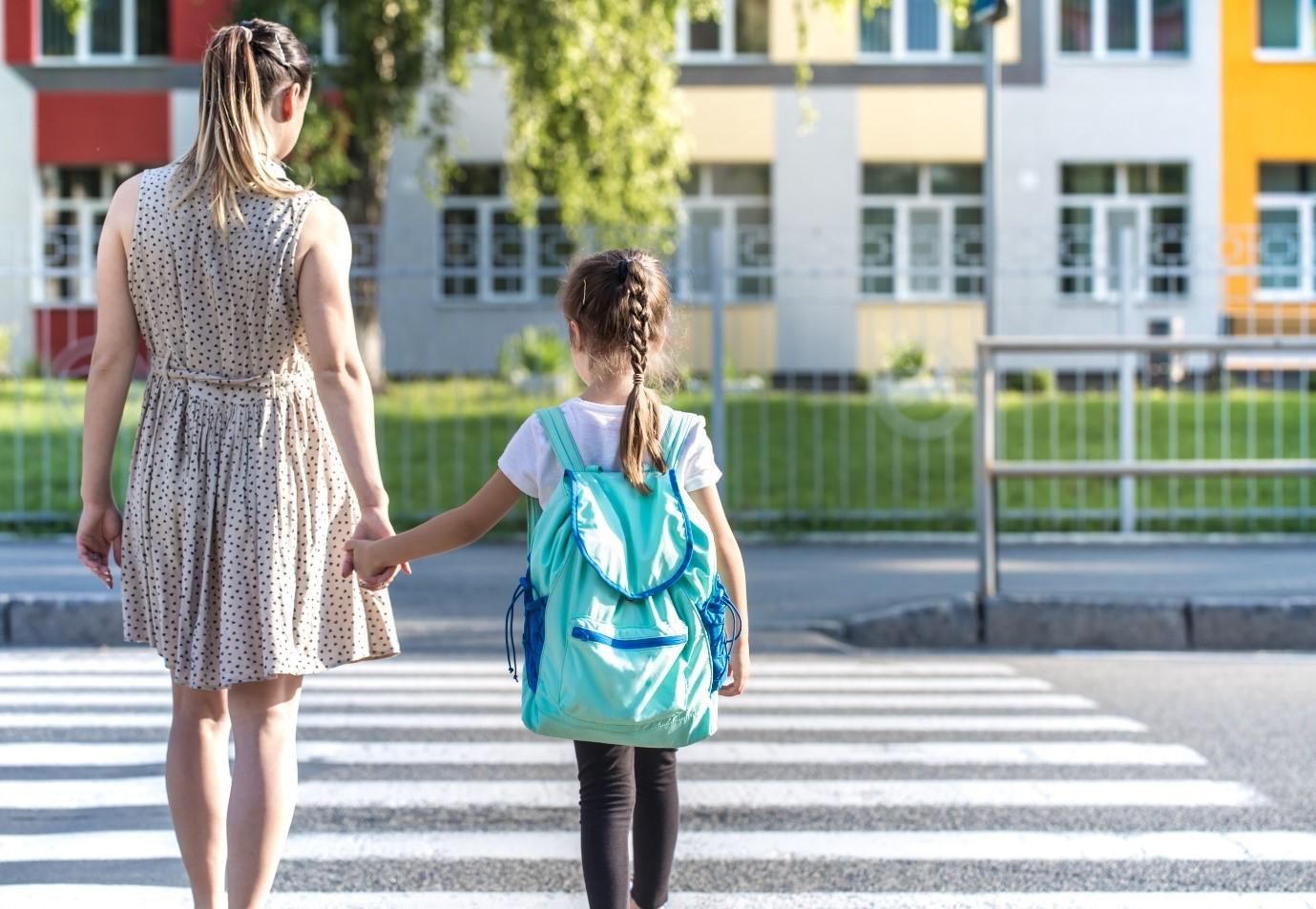 A parent holding a student’s hand about to cross at the pedestrian crossing.