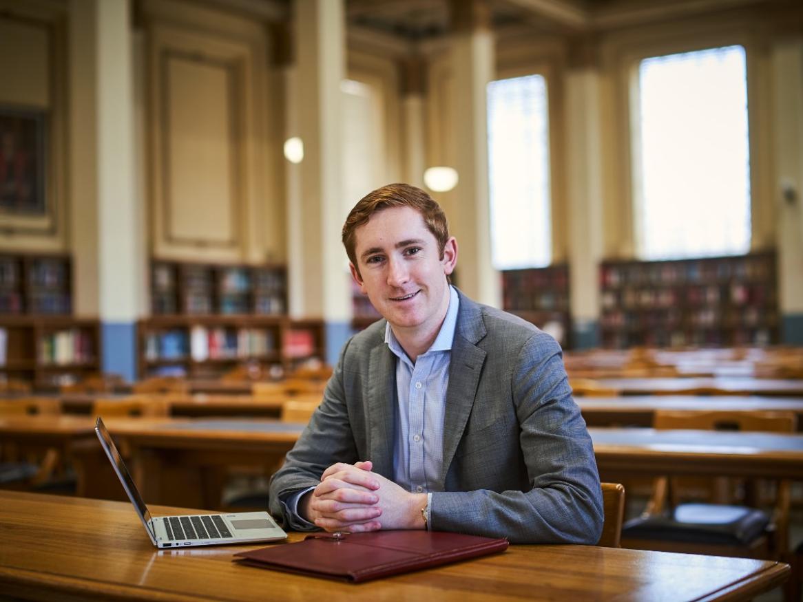Leighton McDonald-Stuart is seated clasping his hands in the library